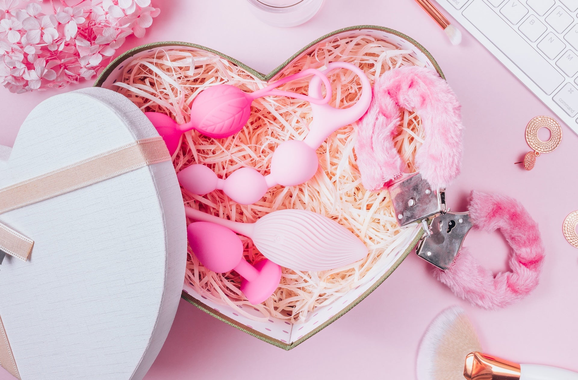 Heart-shaped gift box filled with pink adult toys and fluffy handcuffs displayed on a soft pastel background for Seductiva NZ
