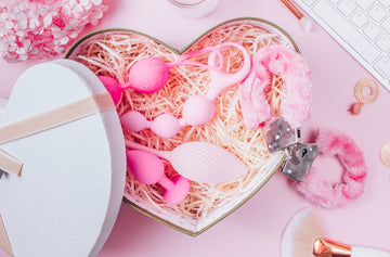 Heart-shaped gift box filled with pink adult toys and fluffy handcuffs displayed on a soft pastel background for Seductiva NZ
